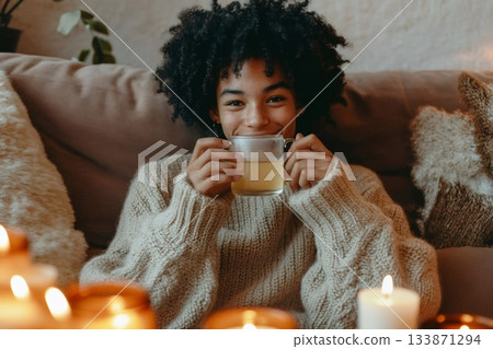 Person smiling and drinking herbal tea, creating a relaxing and comforting atmosphere with lit candles at home Person smiling and drinking herbal tea, creating a relaxing and comforting atmosphere with lit candles at home 133871294