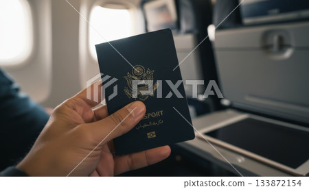 Traveler's hand holding a blue united states passport inside an airplane cabin, preparing for an international flight and global journey to a vacation destination 133872154