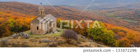 Stone church standing on a hilltop, overlooking a vast valley filled with colorful autumn trees, creating a serene and picturesque landscape 133872296