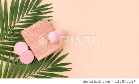 Soft pink spa items arranged with green palm leaves on a light peach background for a relaxing atmosphere 133873154