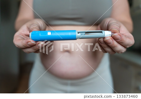 GLP-1 injection pen held by woman in front of abdomen, weight management concept 133873460