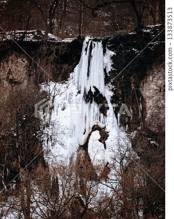 Frozen Waterfall In Bad Urach, Baden Wuerttemberg: Dramatic Winter Ice Formations With Icicles And Snow Covering Rocks And Bare Trees 133873513