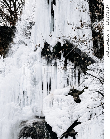 Frozen Waterfall In Bad Urach, Baden Wuerttemberg: Dramatic Winter Ice Formations With Icicles And Snow Covering Rocks And Bare Trees 133873537