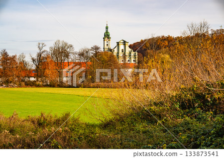 Historic Fuerstenfeldbruck Monastery In Bavaria: Baroque Church Tower Rising Above Autumn Trees And Open Green Fields Under Soft Daylight Historic Fuerstenfeldbruck Monastery In Bavaria: Baroque Church Tower Rising Above Autumn Trees And Open Green Fields Under Soft Daylight 133873541