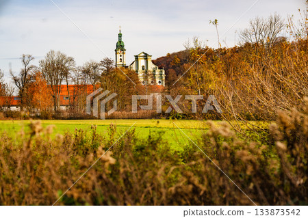 Historic Fuerstenfeldbruck Monastery In Bavaria: Baroque Church Tower Rising Above Autumn Trees And Open Green Fields Under Soft Daylight 133873542