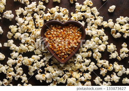 Popcorn in a brown wooden plate in the shape of a heart on a wooden table. Popcorn in a brown wooden plate in the shape of a heart on a wooden table. 133873627
