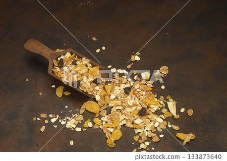 Beakfast cereals in wooden spoon. Healthy muesli with oat flakes, nuts and raisins isolated on dark Beakfast cereals in wooden spoon. Healthy muesli with oat flakes, nuts and raisins isolated on dark 133873640