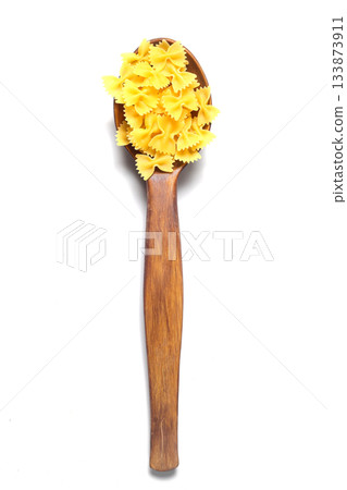 Raw pasta farfalle on wooden spoon on White background. Top view of Italian cuisine ingredient. Raw pasta farfalle on wooden spoon on White background. Top view of Italian cuisine ingredient. 133873911