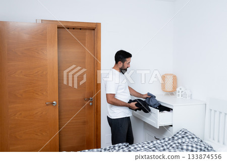 Young hispanic male organizing clothes in bedroom dresser near wooden doorway Young hispanic male organizing clothes in bedroom dresser near wooden doorway 133874556