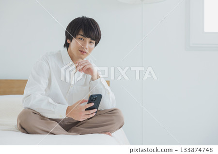 年輕人在臥室裡看智能手機 133874748