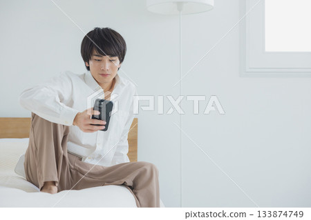 年輕人在臥室裡看智能手機 133874749