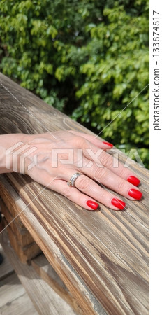 A woman's hand with a wedding ring and red manicure lying on a wooden railing 133874817