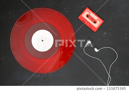 Red Audio cassette and Red vinyl record on a black background. Retro style. Top view. With White headphones . Red Audio cassette and Red vinyl record on a black background. Retro style. Top view. With White headphones . 133875395