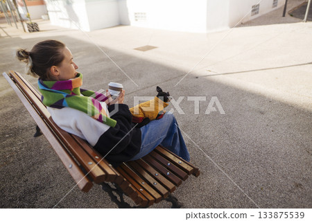young woman on bench holding coffee, freelance writer break young woman on bench holding coffee, freelance writer break 133875539