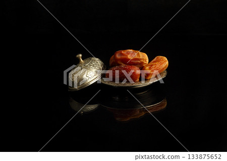 Dried dates on a wooden table in silver dishes close-up. Composition of dried dates in ramadan dish Dried dates on a wooden table in silver dishes close-up. Composition of dried dates in ramadan dish 133875652