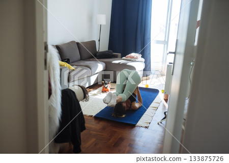 caucasian woman folding into restorative pose with pet nearby 133875726