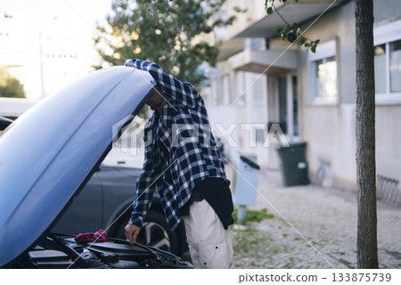 Young man in flannel reviews engine and battery prior to busy delivery day 133875739