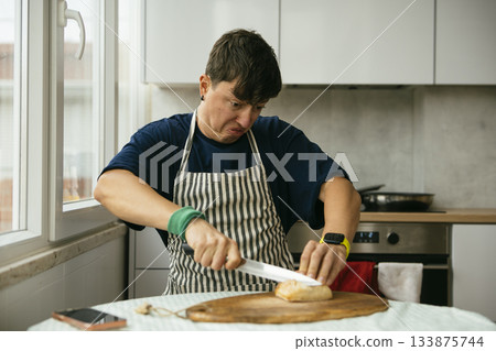 Person in striped apron precisely cuts sourdough bread in sunny kitchen Person in striped apron precisely cuts sourdough bread in sunny kitchen 133875744