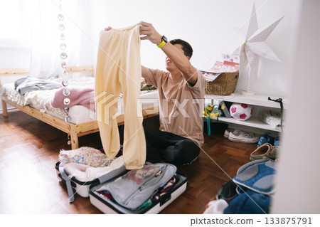 Young man carefully arranging belongings for travel in sunlight 133875791