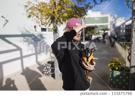 Man prevents sunlight glare during city stroll with pet 133875798