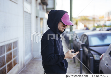 Casual urban figure inspecting rideshare application near parked vehicles 133875827