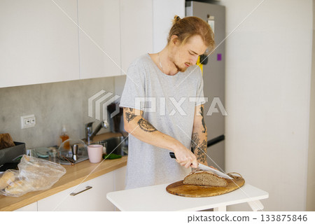 Trimmed for safety, Man cuts sourdough bread amid rustic setting 133875846