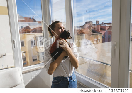 Young woman happily lifts her small dog during cheerful moment 133875903