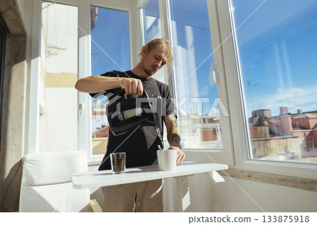 Young man seems to be setting up busy workday with coffee and city view 133875918