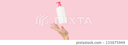 Womans hand holding white bottle on pastel pink background 133875949