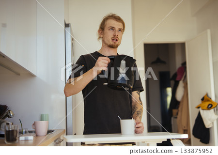 Indoor scene of young man pouring hot beverage into mug 133875952