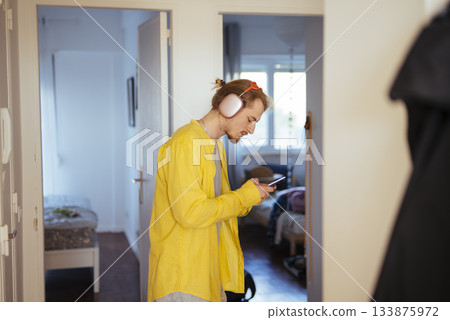 Relaxed individual checking phone amid apartment corridor ambiance Relaxed individual checking phone amid apartment corridor ambiance 133875972