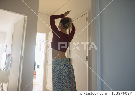 Bright corridor pause, Serene woman stands with hand on head 133876087