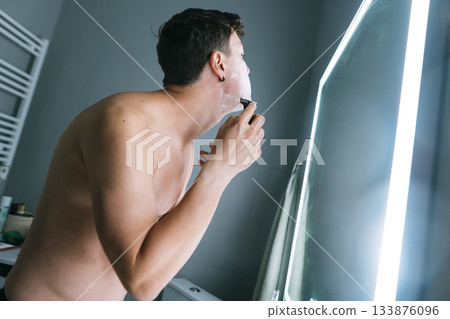Focused man grooming facial hair with steady electric shaver movement Focused man grooming facial hair with steady electric shaver movement 133876096