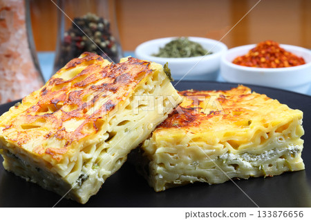 Slices of baked Round Borek cheese pie in kitchen tray with herbs. Dark background. Top view. Copy space 133876656