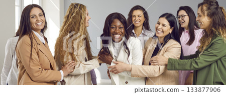 Happy group of young women friends looking at camera and hugging on grey background. 133877906