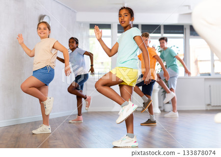 Positive juvenile girl engaged in Hip-hop dance in training room with children's group Positive juvenile girl engaged in Hip-hop dance in training room with children's group 133878074