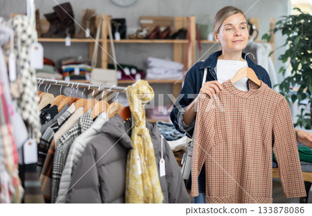 Adult woman chooses warm dress in clothing store Adult woman chooses warm dress in clothing store 133878086