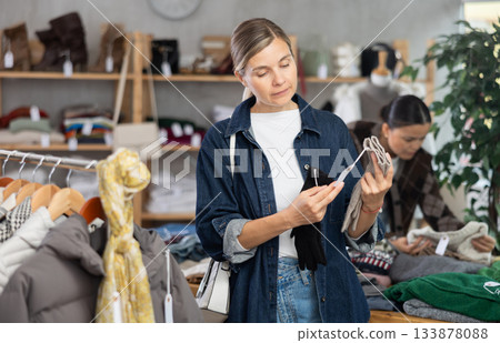 Focused young woman choosing warm gloves for autumn-winter season in clothing shop 133878088