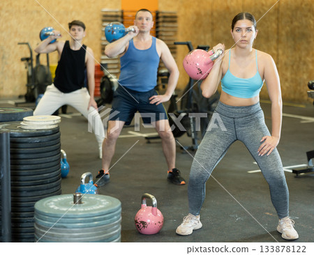 Sportive strong young female in activewear swinging kettlebell during group exercise class in health center indoors 133878122