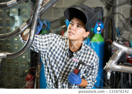 Female welder welding metal pipe structure in workshop 133878142