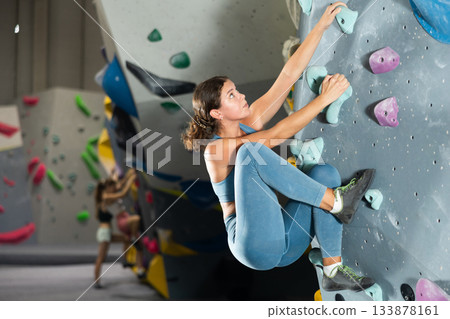 Girl climbs artificial wall bouldering, working out in gym Girl climbs artificial wall bouldering, working out in gym 133878161