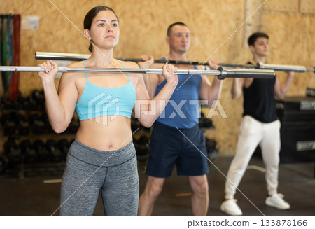 Sporty young girl doing exercises with barbell in gym Sporty young girl doing exercises with barbell in gym 133878166