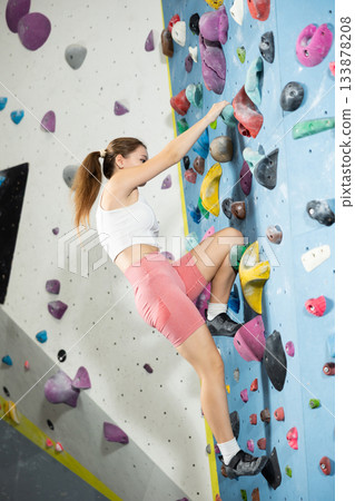 Sportive girl climbing on artificial rock wall in rock climbing gym Sportive girl climbing on artificial rock wall in rock climbing gym 133878208