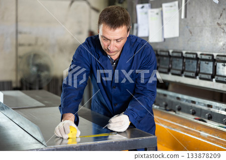 Portrait of worker with tape measure who measures sheet of iron using tape measure and marks cutting line Portrait of worker with tape measure who measures sheet of iron using tape measure and marks cutting line 133878209