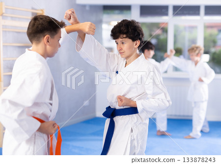 Karate kids in kimono sparring together during their group karate training in modern sports gym Karate kids in kimono sparring together during their group karate training in modern sports gym 133878243