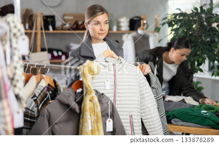 Attractive female customer chooses autumn down jacket in clothing boutique Attractive female customer chooses autumn down jacket in clothing boutique 133878289