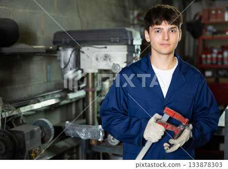Young technician with clamp in hands posing in metal workshop 133878303