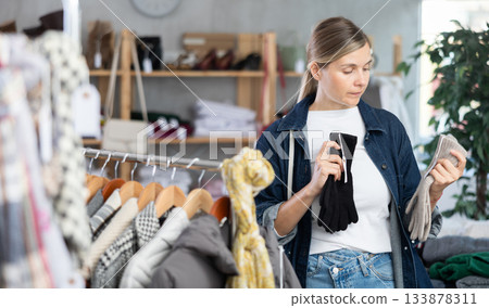 Focused young woman choosing warm gloves for autumn-winter season in clothing shop 133878311
