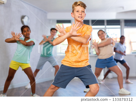 Positive juvenile boy engaged in Hip-hop dance in training room with children's group Positive juvenile boy engaged in Hip-hop dance in training room with children's group 133878312