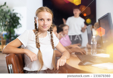 Smiling preteen girl sitting at computer table in training room 133878360